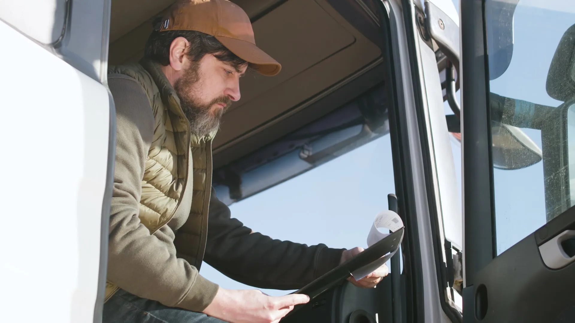 A truck driver in the cab reviews paper documents before leaving.