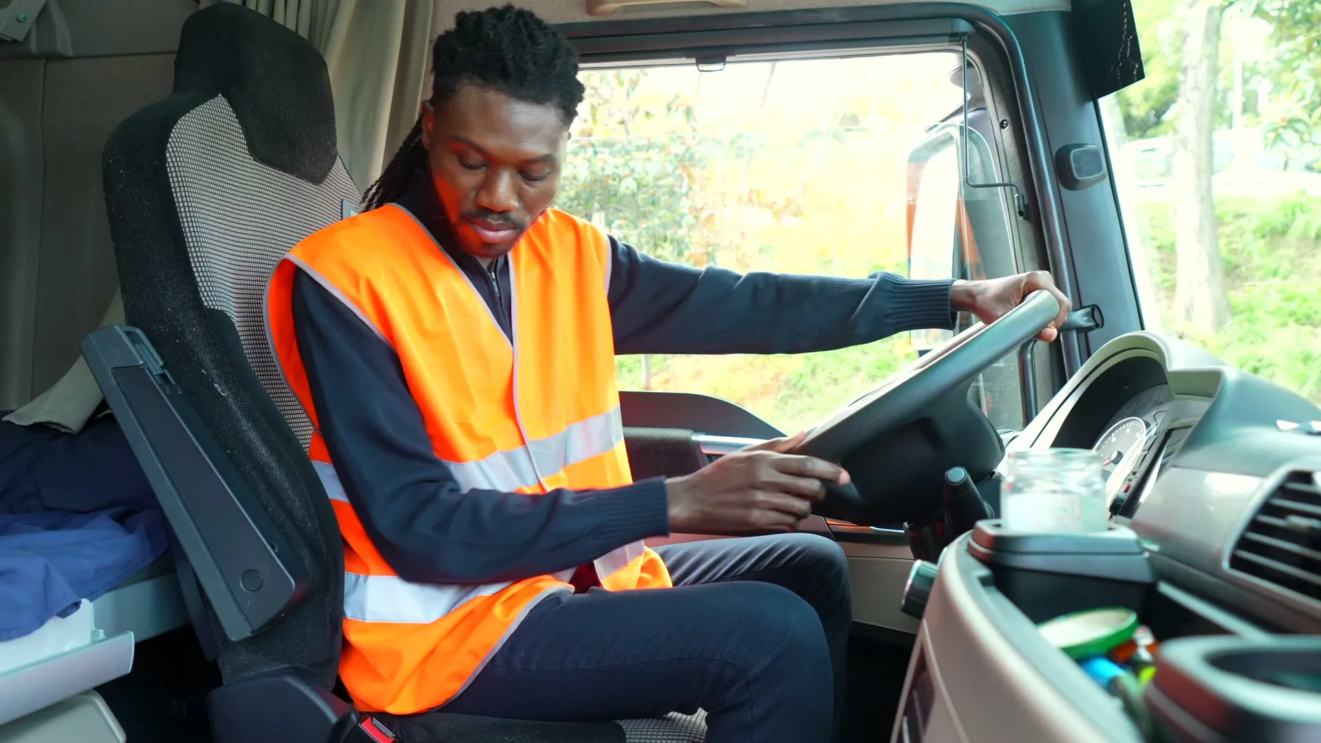 A driver in an orange high visibility vest at the wheel of a truck.