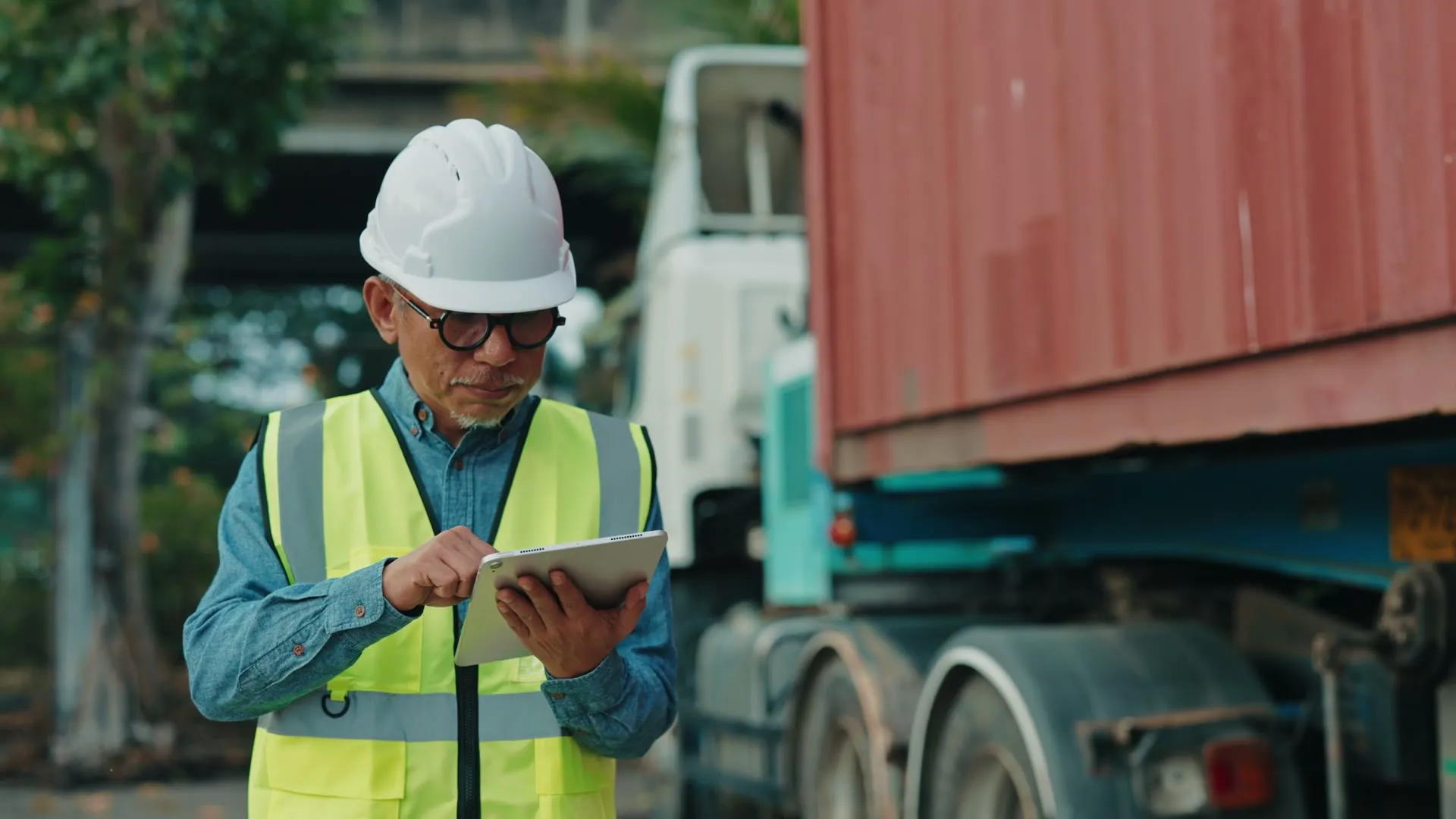 A fleet supervisor in a hard hat and safety vest reviews a tablet next to a truck.